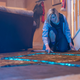 Jodie Whittaker's 13th Doctor examines a blue glowing square outline of energy on a living room's carpeted floor.